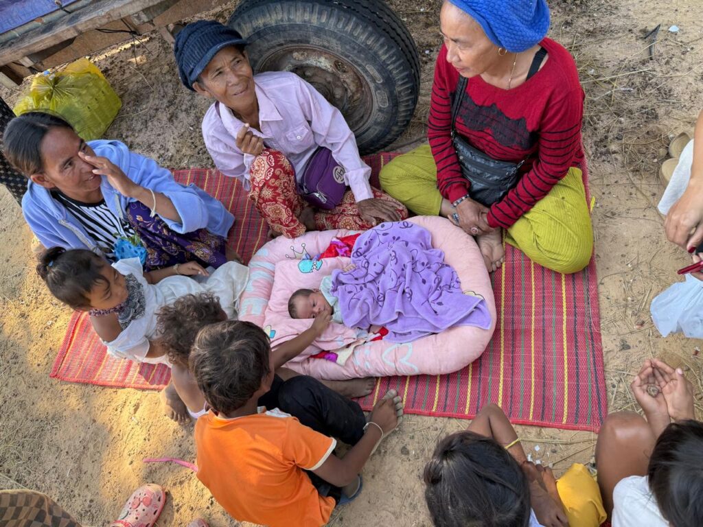 A family gathers to look at a baby that was born in an ad hoc camp site along National Road 68 in Cambodia's Siem Reap province on December 17, 2025. (Mech Dara/Mekong Independent)