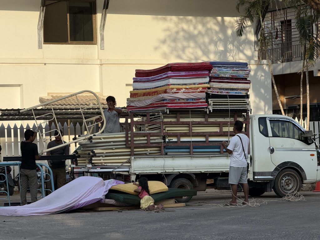A group of men packs bed frames into a truck while a young girl plays on a stack of mattresses taken out from a building near the Koh Kong Resort in Cambodia's Koh Kong province on January 25, 2026. (Mech Dara/Mekong Independent)