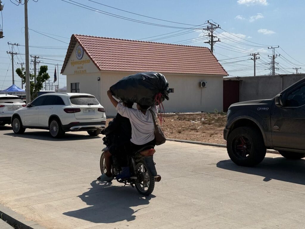 Two people drive a motorbike while hauling a black trash bag over their head during a police raid in A7 Park in Cambodia's Bavet city on February 1, 2026. (Mech Dara/Mekong Independent)