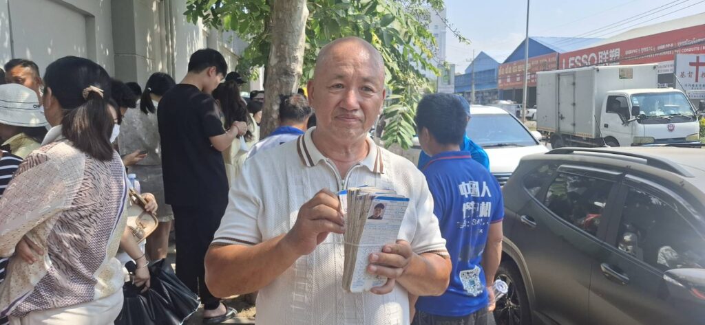 Wang Xijun, a construction company manager, holds up the paycards of 78 construction workers that he says he can't pay because of the freezing of Huione and H Pay services, at the National Bank of Cambodia headquarters in Phnom Penh on April 7, 2026. (Danielle Keeton-Olsen/Mekong Independent/Creative Commons)