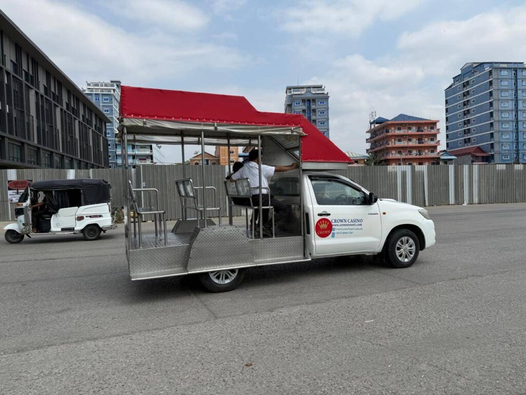 A truck labeled "Crown Casino" drives two people in white shirts through the streets of Poipet city on April 30, 2026. (Mech Dara/Mekong Independent/Creative Commons)