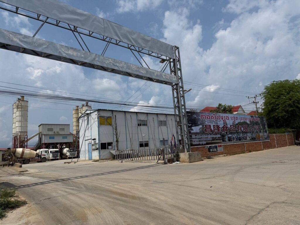 Cement trucks and cement-making cylinders are visible from the entrance of Cangxinlong Food (Cambodia) complex in Pailin province's Stung Kach commune on May 7, 2026. (Mech Dara/Mekong Independent/Creative Commons)