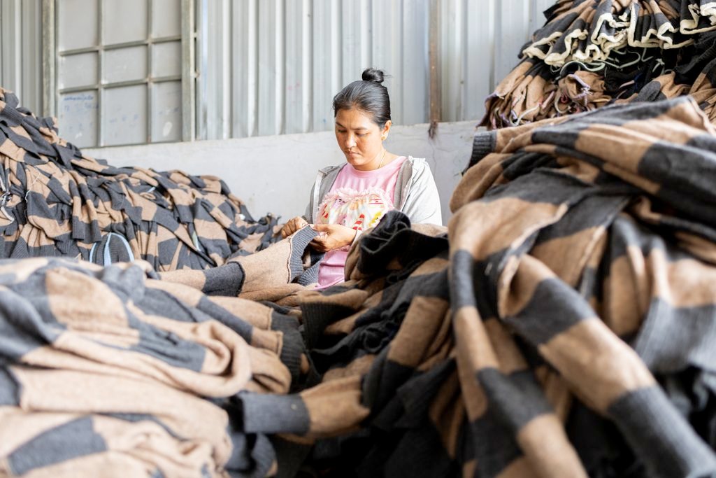 A garment worker in a subcontracted factory inspects products piled around her in Phnom Penh on May 19, 2026. (Mech Choulay/Mekong Independent/Buy photos from Choulay)