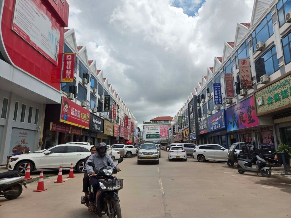 Cars and motorbikes drive along a street in the Xang Jieng Market, also known as "Chinatown", in Vientiane city, where many businesses prominently advertise in Chinese language, in late July 2026. (Apichart Sopapong/Mekong Independent)
