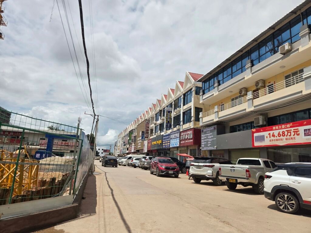Cars park along a street in SanJiang Market, also known as the "Chinatown" area of Vientiane city, where many businesses prominently advertise in Chinese language, in late July 2026. (Apichart Sopapong/Mekong Independent)